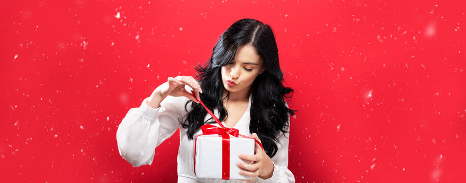 Happy Young Woman Opening A Christmas Gift Box On A Red Background