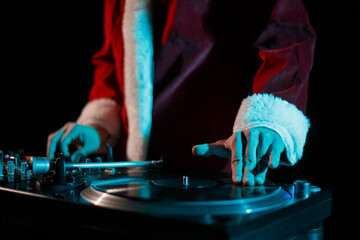 Hip hop dj in Santa outfit scratches vinyl record on turntable. Disc jockey plays music on...