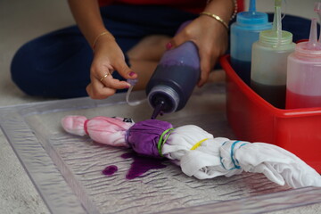 Little kid enjoying making a craft, using different colour ink to paint a tie-dyed cloth. Kids arts...