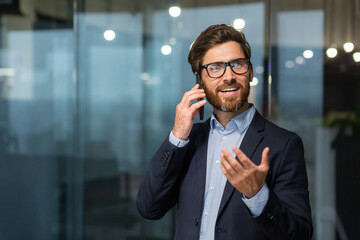 Mature businessman in a business suit talking on the phone, the manager is satisfied with the result of the achievement and work talks about the positive result, the man is at work inside the office.