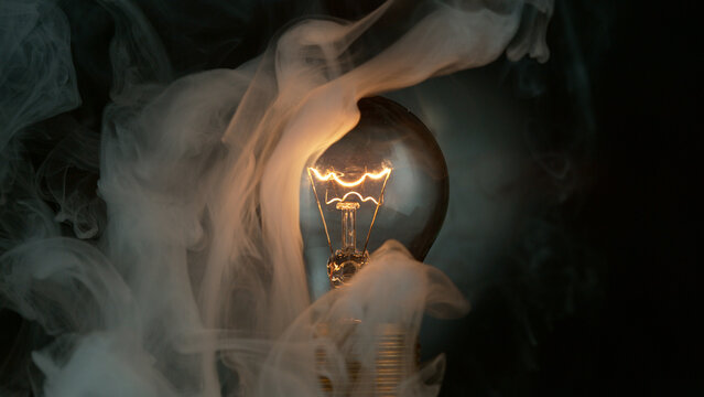 Close-up of shining light bulb with smoke, dark background