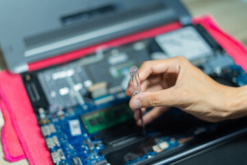 Soft focus, hand is using a screwdriver to tighten the nut. To change the battery of a notebook computer by yourself. Changing electronic devices by yourself concept..