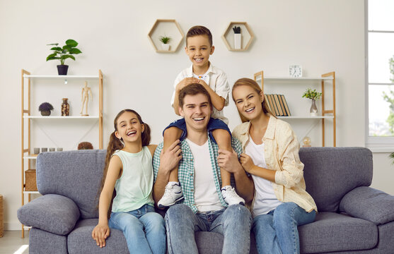 Happy family of four having fun at home. Portrait of cheerful, joyful, beautiful parents and children sitting together on the sofa in the living room, looking at the camera and laughing