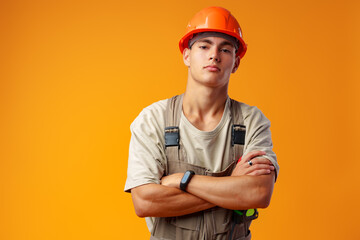 Young construction worker in helmet and uniform posing on yellow background in studio