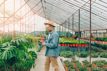 Obraz premium Smiling gardener young man talking on phone in greenhouse. Concept owner small business of sale flowers