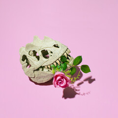 Dinosaur skull with flower in the mouth, creative floral layout against pastel pink background. 