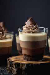 Layered dessert Trifles in a transparent glass.  Sponge biscuit and three chocolate mousse layers. Chocolate souffle trifle cake in individual disposable transparent cups. Black background