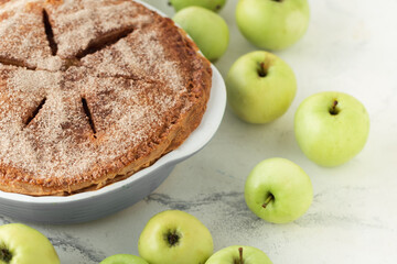 Homemade apple pie on the white marble background with cinnamon flavor covered with sugar Flaky Crust surrounded by green apples.
