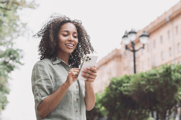 Young beautiful woman using smartphone in a city. Smiling student girl texting on mobile phone outdoor. Modern lifestyle, connection, casual business concept