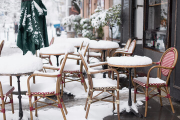 Snowy winter scene on beautiful city street, Cafe tables covered with snow in old European town, Outdoor restaurant terrace at cold snowy day
