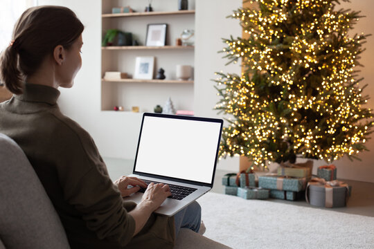 Young woman using laptop computer with blank empty mockup screen during Christmas holidays at home, Online shopping at winter holidays, ordering Christmas gift, Website template