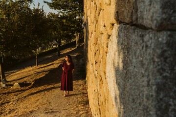 Young caucasian lady walking near the wall of the Castle of Longroiva, Portugal at sunset