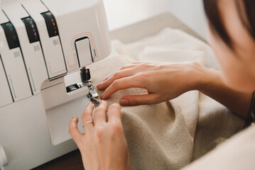 Woman's hands using a sewing machine to sew fabric, or curtains, or clothes.
