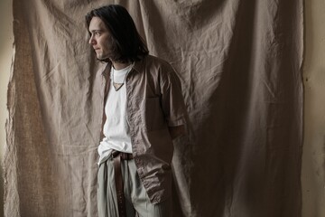 Naklejka premium Aesthetic shot of a handsome young man in silk clothing against a beige background