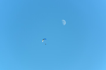 Paramotor in flight on a sunny day with the moon in the sky.