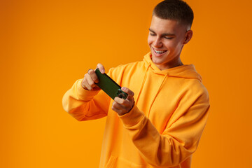 Fototapeta na wymiar Portrait of excited young man playing online game on mobile phone on yellow background.