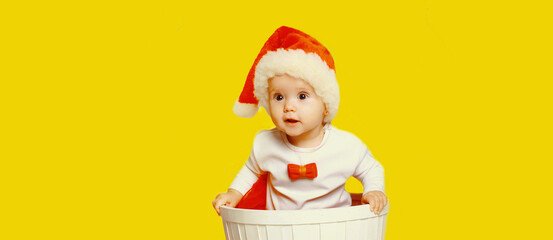 Portrait of happy smiling little child in christmas santa red hat playing with toys on yellow background