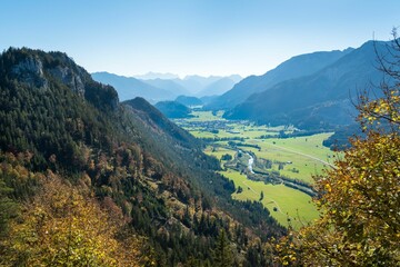 Aerial view of a river in a green meadow surrounded by high mountains on a sunny day