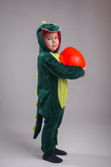 A boy dressed as a Tirex is holding a dinosaur egg.
A child in a dinosaur costume on a white background.