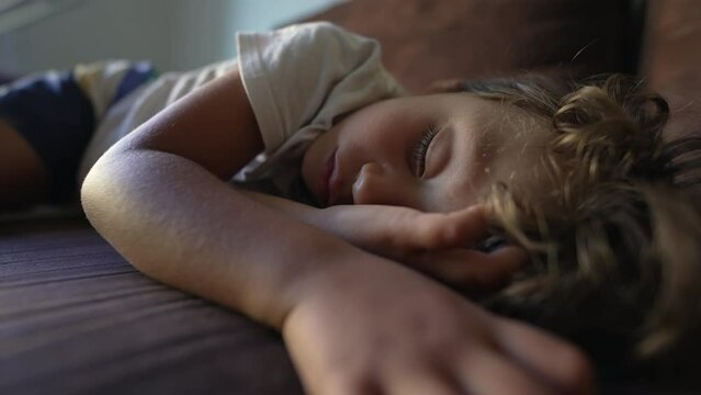 Sleeping child lying on couch napping. Kid in deep slumber asleep during afternoon nap. Cute tired little boy resting