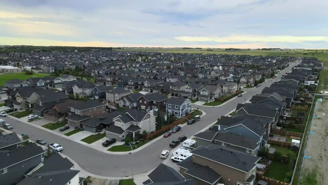 Drone footage over residential neighborhood, buildings with gray roofs and yards in Airdrie, Canada.