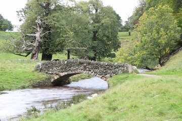 River with a high stream water flood from a canal with a small bridge in a greenfield