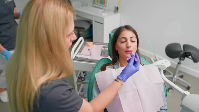 Woman Professional Dentist Performs Treatment Procedure on Female Patient in Modern Dental Clinic. Beautiful Orthodontist with Blond Hair Treats Client Teeth. Medicine and Healthcare. Slow motion