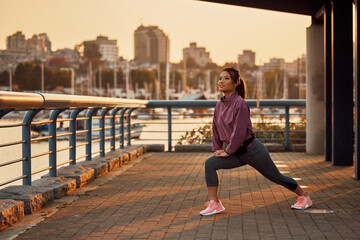 Fototapeta na wymiar Smiling Asian athletic woman stretching her legs while warming up at quay.