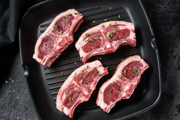 Raw lamb loin rib chops steaks in grill skillet with rosemary and thyme. Black background. Top view