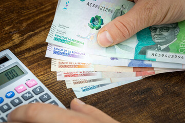Man holds Colombian pesos in hand and counts on expenses or earnings calculator, Financial concept,...
