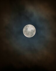 Vertical shot of a bright full moon isolated on the black cloudy sky background