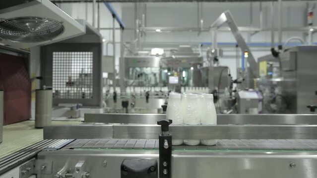 Automated production line at the Dairy Food Facility. Multiple plastic milk bottles are being filled with milk on an automated production line. Pouring milk on automated production line.