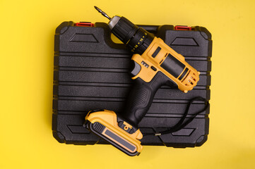 Electric cordless yellow drill driver and an empty black carrying case on a yellow background.