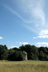 Fototapeta na wymiar Vertical shot of a gazebo between green trees in the meadow under blue cloudy sky