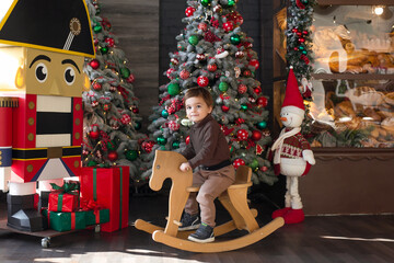 Little happy boy sitting on a toy horse near Christmas tree.