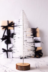 Modern white decorative Christmas tree in front of group of wrapped boxes with presents on white textured backgrond. Place for text.