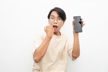 excited young asian man in beige tshirt holding and showing phone screen with happy euphoric shocked wow expression. man pointing to screen phone with thumb up. billboard model advertisment concept.