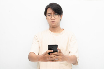 asian young man in casual beige tshirt holding phone with sad, crying, dissapointed expression. bad news from phone concept.