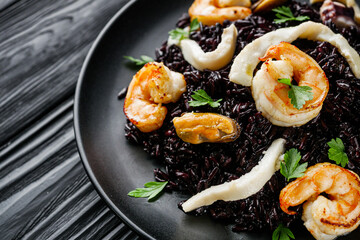 delicious black rice with shrimps and seafood on a black wooden rustic background