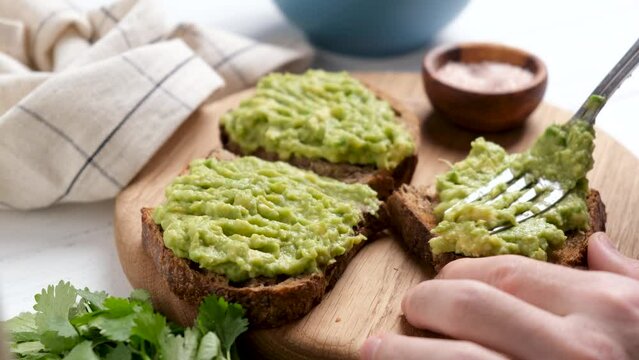 Spread mashed avocado on rye bread toast, closeup view. Healthy vegan food