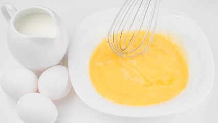 Stirring eggs with whisk. Сhef whisking eggs in white bowl, cooking omelette with milk