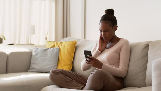 Irritated young black woman reading message on smartphone and typing answer to her boyfriend, tracking shot, free space