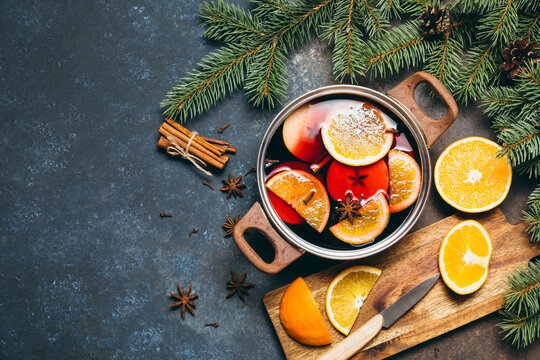 Hot Mulled wine cooking at home for happy christmas time. Red wine, orange, apple and spices - ingredients boiling in a pot on dark background. Warming new year and holiday drink, flat lay.