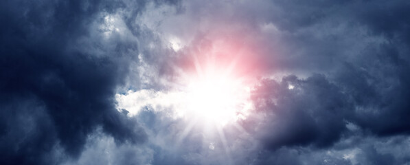 A picturesque dark stormy sky with dense clouds through which the sun peeks through. The sun in a dark cloudy sky