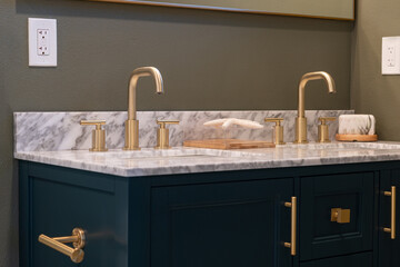 Modern bathroom vanity details of gold faucets and hardware with marble counter, dark blue cabinets...