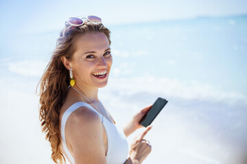 smiling woman at beach sending text message using smartphone