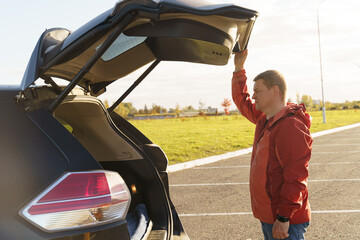 A successful driver opens the trunk of a car while planning a trip.