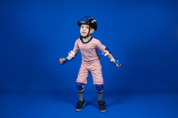 A happy boy in a protective helmet, elbow pads and gloves on a blue background. Protection when riding a bicycle, skateboard, roller skate