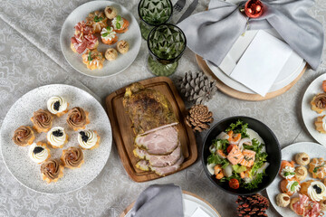Different traditional food for the New Year's table, decorated with balls and fir cones. Russian salad, pastries, appetizers and boiled pork.