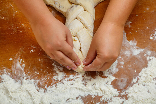 The hands of a Jewish woman weave challah with a pigtail for Shabbat on a wooden table in flour.